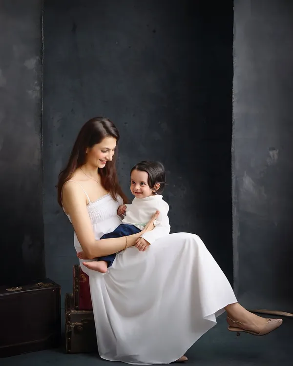 A mother and her child share a gentle moment against a dark, textured backdrop. This painterly style emphasizes emotion and connection, creating a portrait with depth and artistic quality.