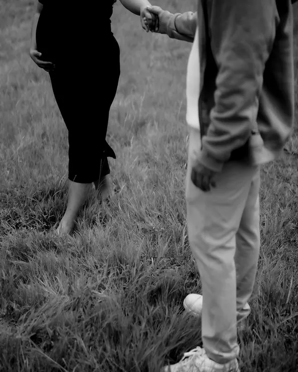 A minimalist black and white shot focusing on the couple holding hands. The simplicity of the image draws all attention to their connection and the baby bump.
