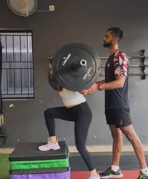 Perfecting the weighted step-up. A coach stands by to ensure flawless form and safety as this client builds single-leg strength and stability, a crucial component of a balanced lower-body program.