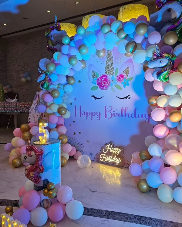 A magical Unicorn-themed 5th birthday party, featuring a large backdrop, a pastel and gold balloon garland, and a light-up 'Happy Birthday' sign.