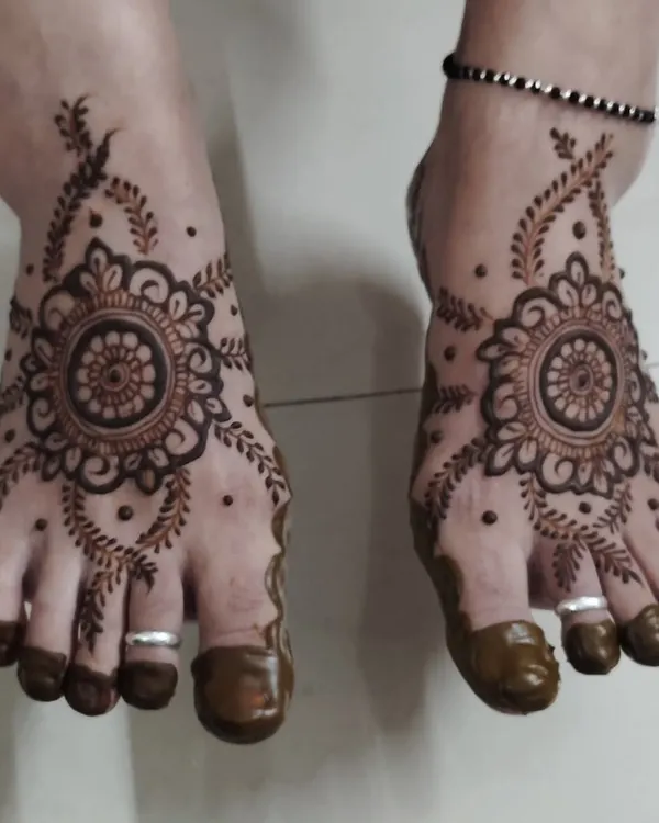 A classic and elegant foot mehndi design. The central mandala is surrounded by delicate leafy vines, and the toes are fully covered for a traditional finish.