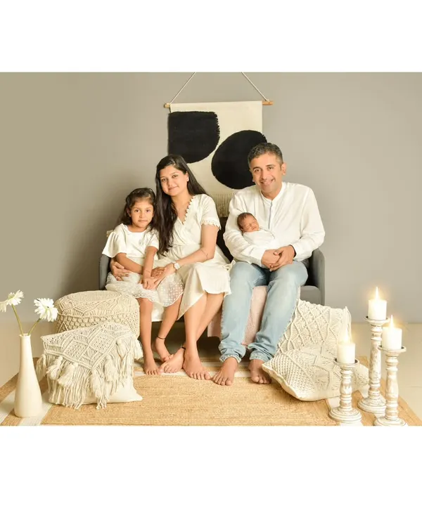 A serene family portrait with a modern, bohemian aesthetic, featuring parents and their two children in coordinating white outfits against a backdrop of neutral tones and textures.