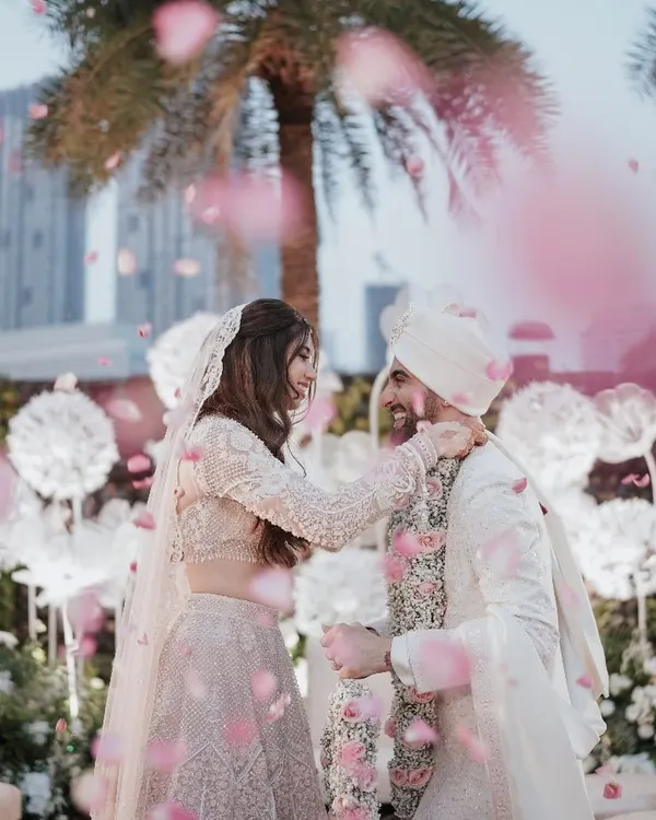 A moment of pure cinematic romance. Rose petals shower the couple as they share a joyful, loving glance during their varmala ceremony, creating a perfect, fairy-tale image.