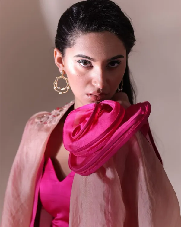A striking portrait where the styling is built around the accessories. The bold, sculptural pink shoulder detail and oversized gold earrings are the focus, complemented by a sharp, winged eyeliner to create a high-fashion look.