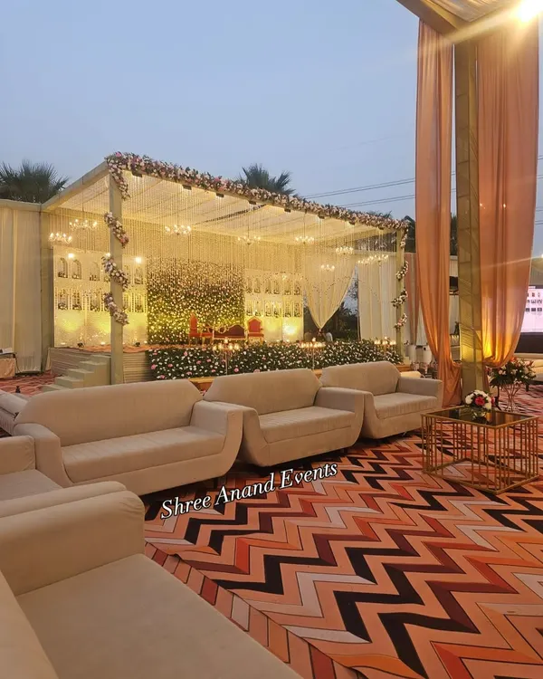 An elegant stage setup with a beautiful floral wall, framed by sheer drapes and illuminated by hanging lights and candles for a soft, romantic glow.