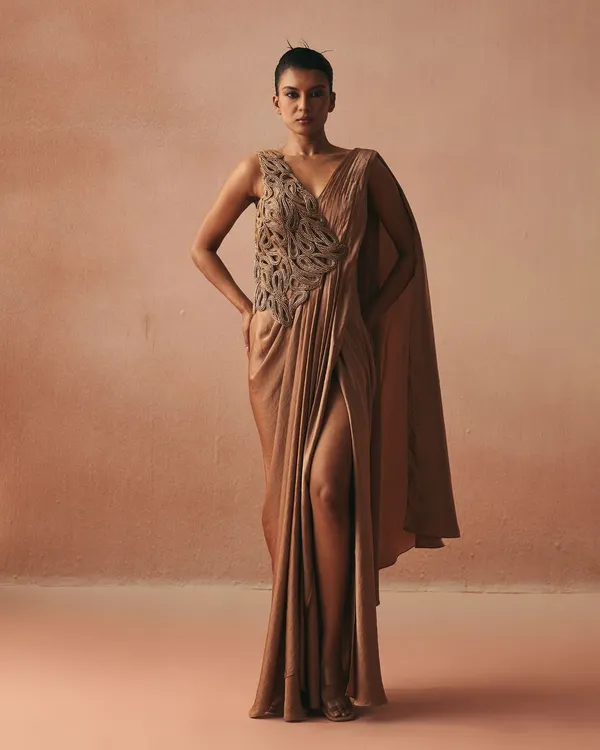 A modern interpretation of the sari, this draped gown in a muted gold tone features a thigh-high slit and a single flowing cape. The bodice is adorned with our signature cord work.