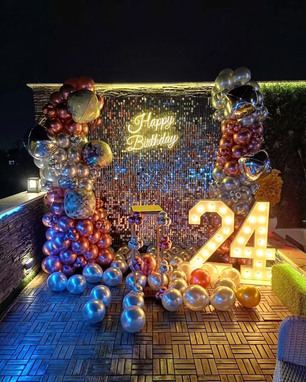 A full view of the shimmer sequin wall decoration, perfect for a milestone birthday party. This setup combines the sparkling backdrop with marquee numbers, a neon sign, and a dense, multi-colored balloon arrangement to create a vibrant photo corner.