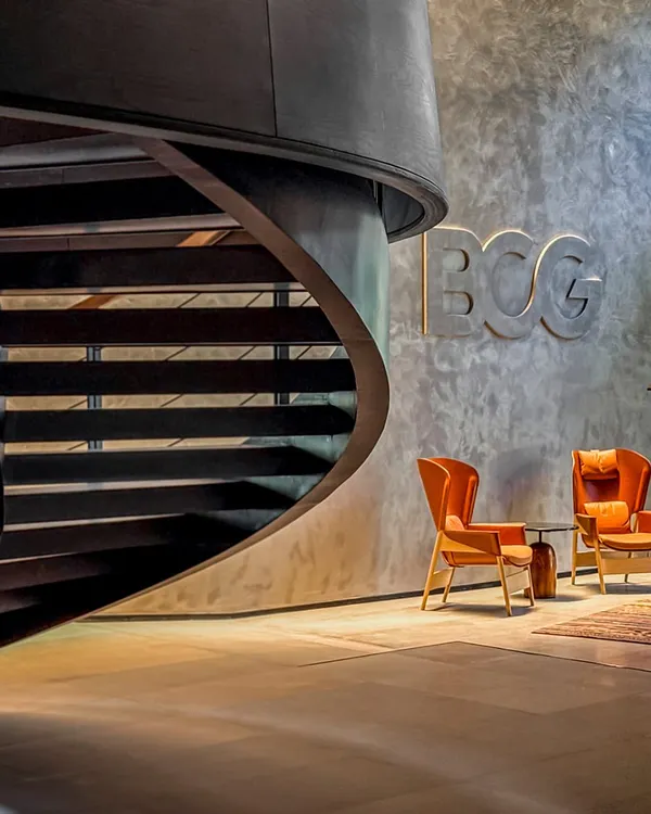 The lobby of the BCG Headquarters in Mumbai features a dramatic spiral staircase set against textured concrete walls, immediately establishing a departure from the typical corporate aesthetic.