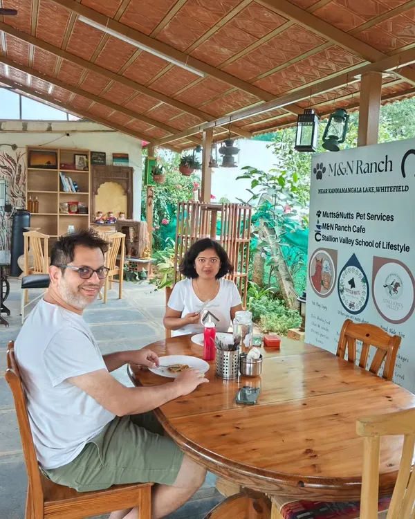 A couple enjoys a peaceful meal at a wooden table in our rustic, covered cafe area. Our space is designed to help you unwind and reconnect with nature, away from the hustle of city life.