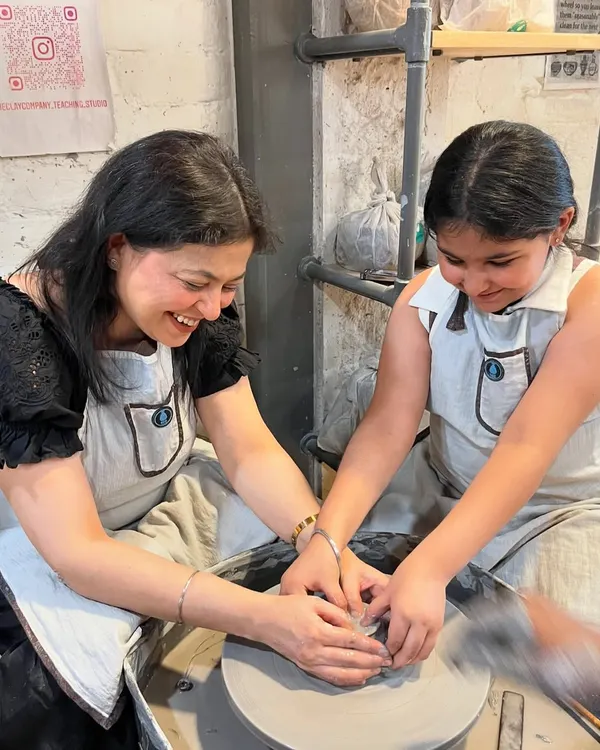 A mother and daughter sharing a smile at the potter's wheel. Our family workshops are designed to create these moments of pure joy and connection.