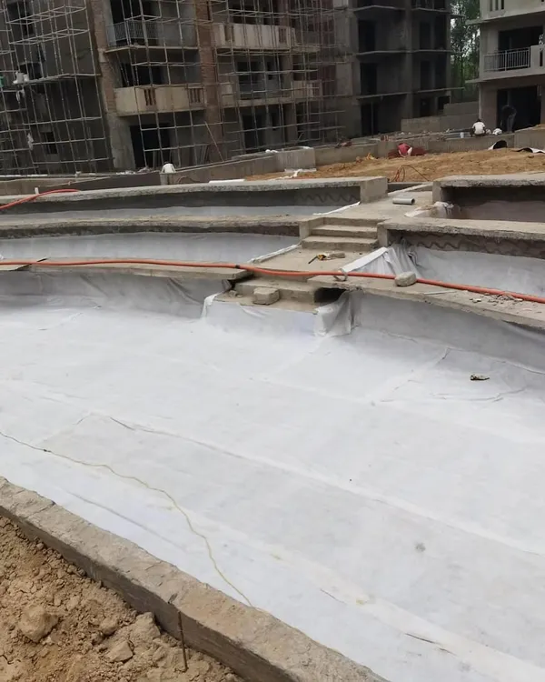 The first step in creating a rooftop or podium garden is waterproofing. Here, we are laying a protective geotextile membrane over the concrete structure.