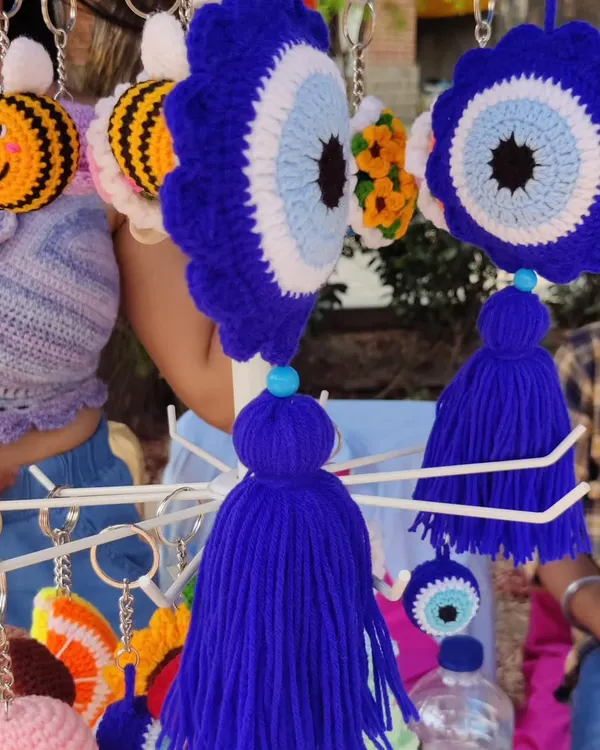My crochet evil eye wall charm hanging at my market stall. This larger "Nazar" charm comes with a tassel and is perfect for hanging on a wall, in a car, or on a door to protect your space.