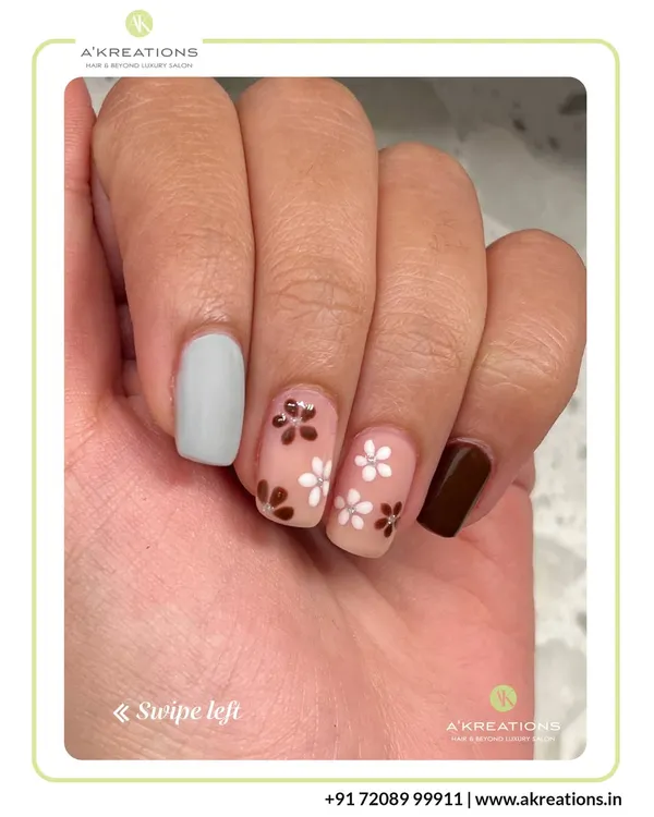 An earthy and chic manicure featuring delicate hand-painted white and brown flowers on a sheer base, complemented by solid grey and brown accent nails.