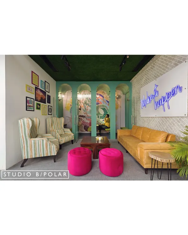 This lounge area in a coworking space we designed uses a mix of colorful furniture, a neon sign, and varied seating to create a welcoming and dynamic environment. The arched glass partitions provide a sense of openness while defining the zone.