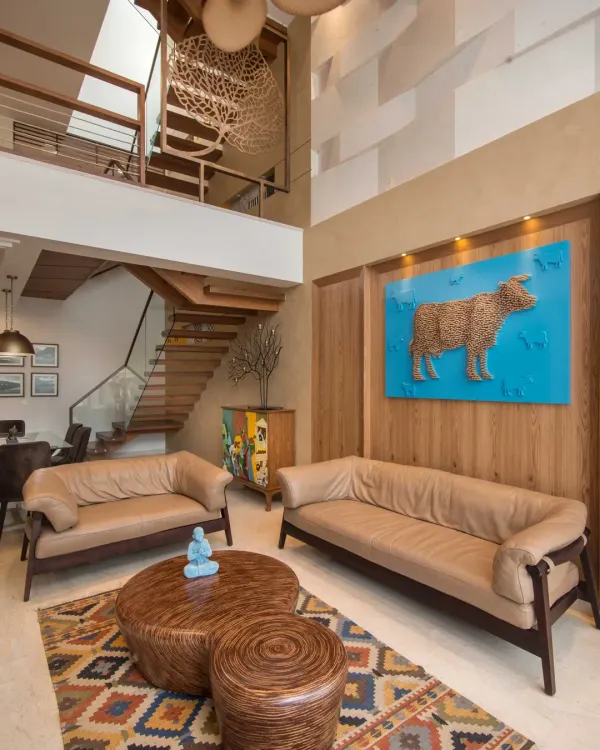 The double-height living area of Kavyam Residence blends warmth and creativity. A bright blue artwork featuring a cow stands out as the main feature, reflecting the client's personal taste and adding a unique, artistic touch to the room.