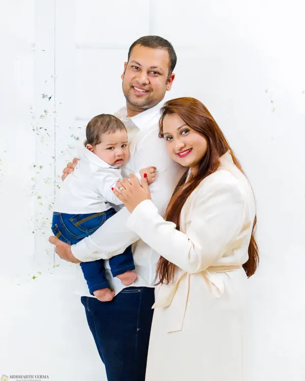 A beautiful, classic family portrait with parents and their baby, all dressed in coordinated white outfits against a clean, bright backdrop. This is a timeless style for any family album.