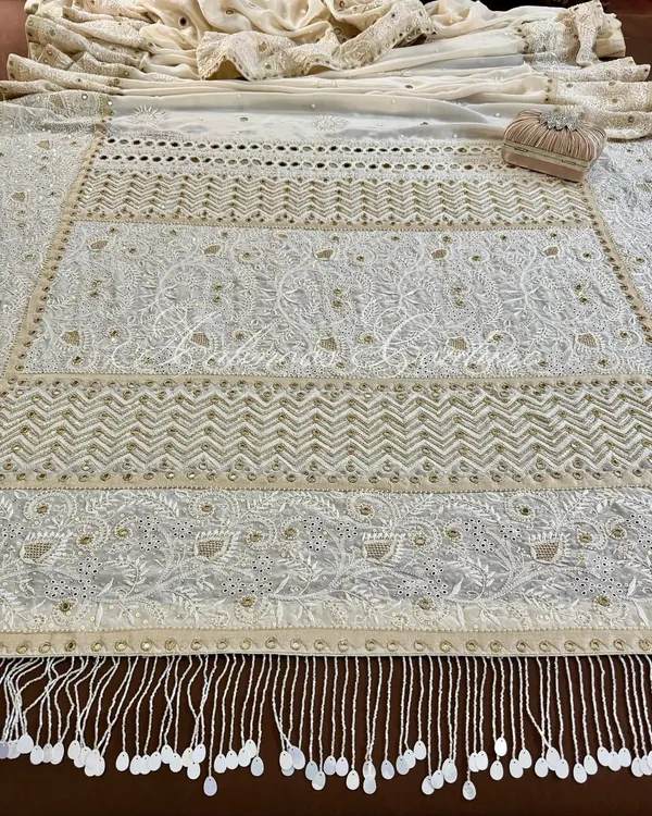 A breathtaking overview of our made-to-order Chikankari saree on off-white crepe. This image showcases the expansive and intricate embroidery, with panels of floral and geometric patterns, and a stunning tassel border.