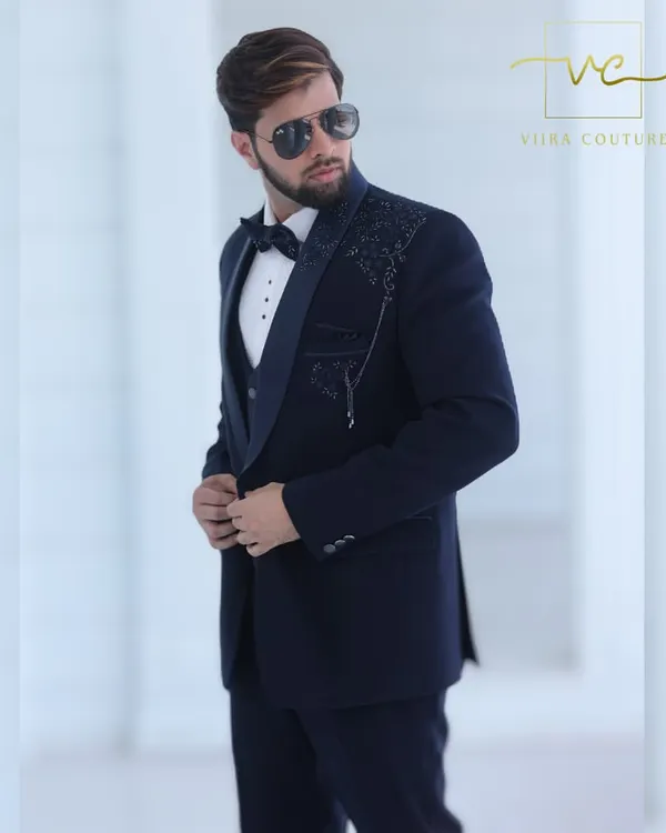 A detailed shot of our custom navy blue tuxedo. The shawl lapel and shoulder are adorned with intricate floral beadwork, adding a layer of texture and sophistication to the deep navy fabric.