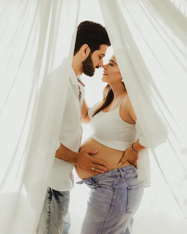 A beautiful, intimate moment from a lifestyle maternity session. The soft, natural light from the window and the casual outfits create a relaxed and authentic feel.