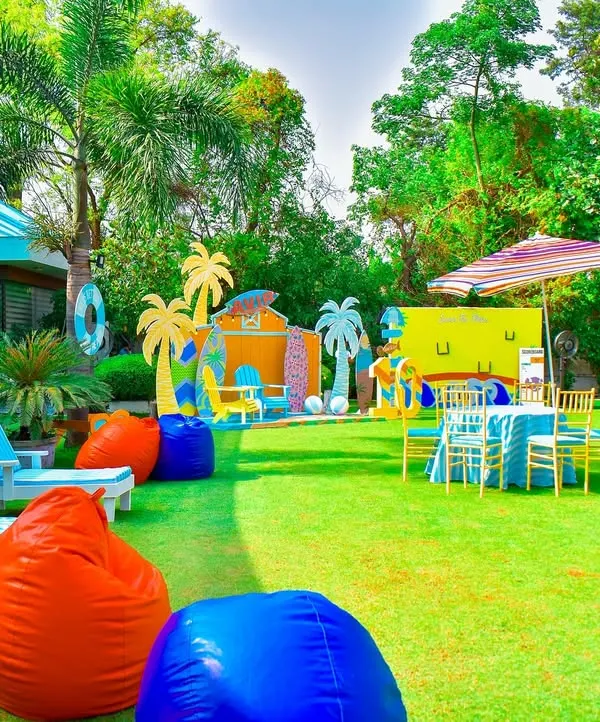 This wide shot showcases a full outdoor summer beach party setup. I used the entire lawn, setting up distinct zones for lounging, photos, and activities, all unified by a vibrant, tropical colour scheme.