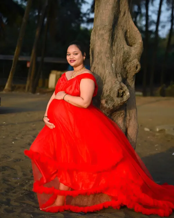 A beautiful outdoor maternity portrait taken at the beach. The vibrant red gown stands out against the natural backdrop, highlighting the baby bump and the mother's radiant smile.