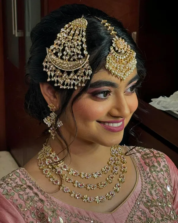 A perfect North Indian engagement look. This bride is wearing a beautiful pink outfit with elaborate kundan and pearl jewellery, including a statement passa and maang tikka. The makeup is soft and rosy to match.