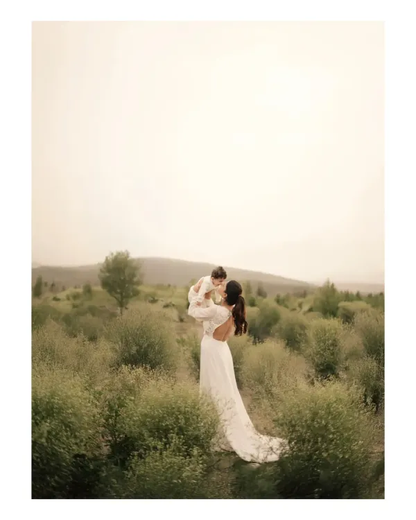 A mother lifts her child towards the sky in a wide, open field. This image captures a feeling of freedom, joy, and boundless love, with the vast landscape emphasizing the grand scale of a mother's affection.