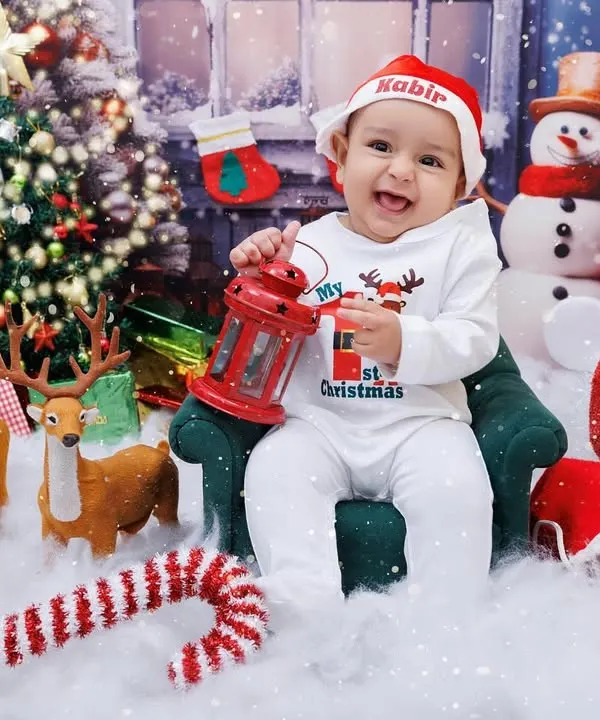 The happiest baby celebrating his first Christmas, holding a lantern in a festive winter wonderland setup.