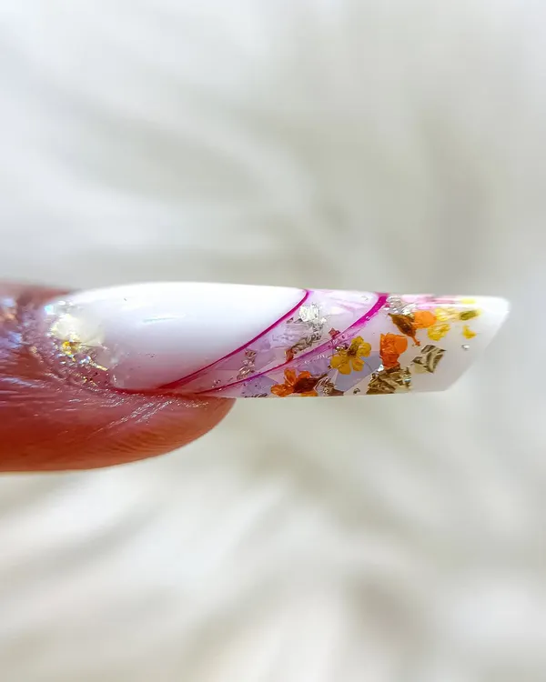 A close-up of an intricate inbuilt nail art design. This technique involves encapsulating dried flowers and foil flakes within the nail extension for a beautiful, dimensional effect.