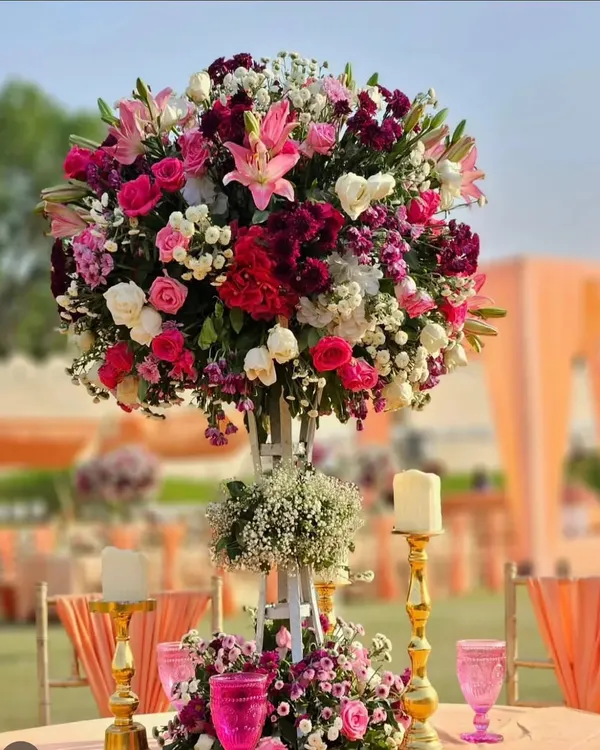 A magnificent and lush floral centerpiece for a VIP table. This arrangement features a rich mix of roses, lilies, and other blooms in shades of pink, white, and burgundy, creating a statement piece.