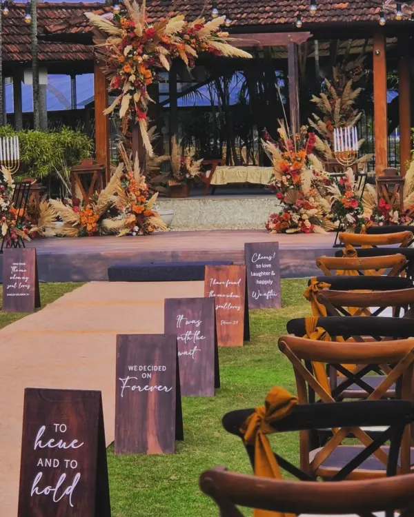 The aisle view of a beautiful boho-themed wedding. I used custom wooden signs with romantic quotes to guide the couple's path to a stunning mandap decorated with pampas grass and autumnal flowers.