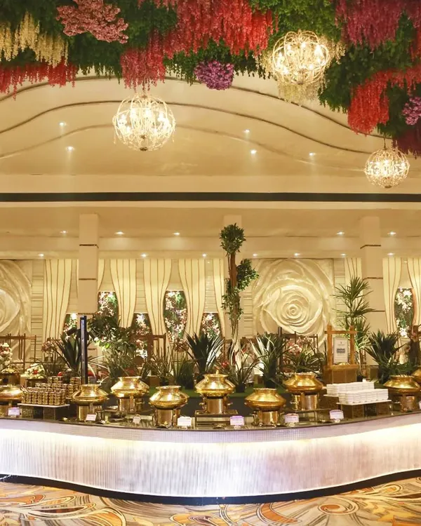 An opulent wedding reception setup featuring a grand, curved buffet line with traditional brass serveware, set under a stunning floral ceiling. This demonstrates our capability for large-scale, luxurious events.
