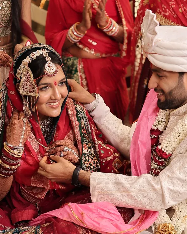 A happy moment from a Marwadi wedding ceremony. The bride's subtle makeup and radiant smile shine through, complementing her traditional red attire and jewelry.