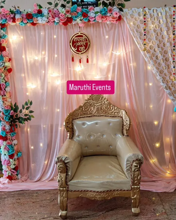 This is a complete backdrop I created for a Jain Tapasvi homecoming. It features a special throne-style chair, a soft pink fabric backdrop with fairy lights, a colorful artificial flower arch, and the sacred "Tapasvi Amar Raho" sign to create a blessed space.