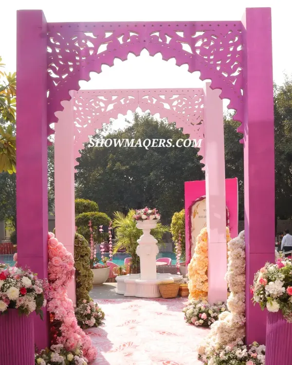 A grand entrance for a pink themed Haldi ceremony, featuring intricately cut magenta arches and lush floral arrangements, creating a stunning poolside welcome.