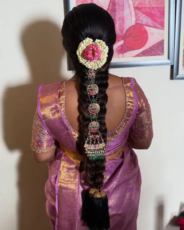 A stunning South Indian bridal braid featuring intricate temple jewelry and a floral heart design made with jasmine and rose petals. This is a perfect example of a traditional yet personalized bridal look.