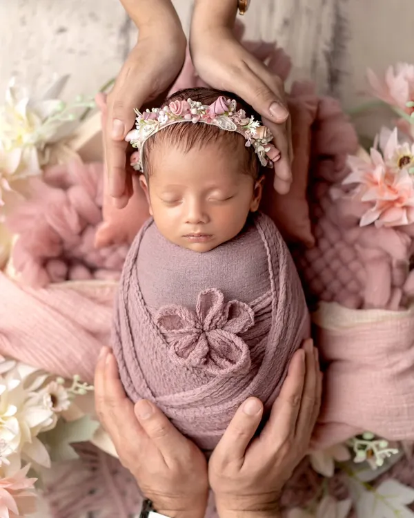 A perfect little angel, wrapped in pink and crowned with flowers. This classic newborn pose, with the baby cradled in parents' hands, is a timeless way to remember how small they once were.