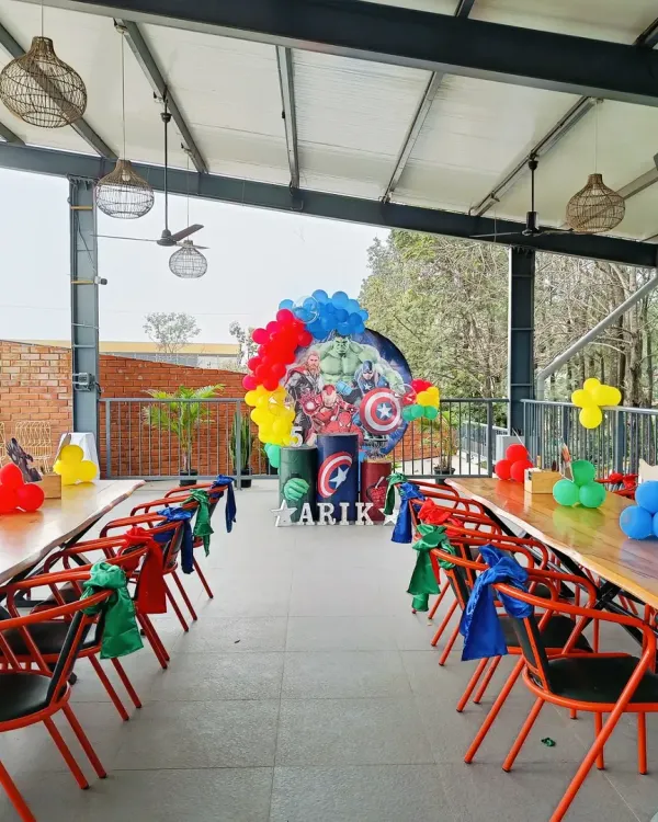 An Avengers-themed party setup in an outdoor venue, showing the main backdrop and themed table arrangements for guests.