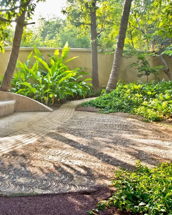 From a past project, this image shows a custom-paved walkway made with local stone. The swirling pattern mimics natural forms and is integrated with a built-in seating area, surrounded by tropical plants.