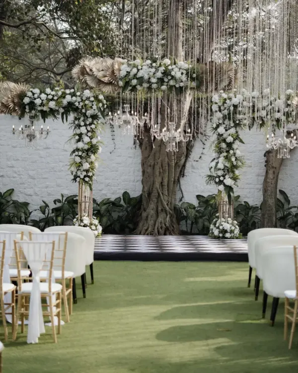 This stunning outdoor wedding ceremony was set against a beautiful old tree, which we framed with an arch of white flowers, greenery, and delicate chandeliers. The checkered dance floor and elegant seating completed this timeless and classic wedding design.