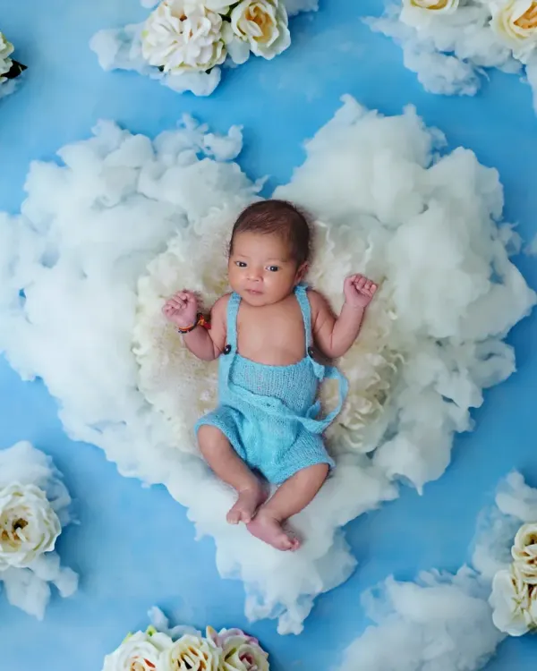 A sweet and serene newborn portrait. I created this image by placing the baby on a fluffy cloud heart, using a soft blue sky and white flowers for a heavenly feel.