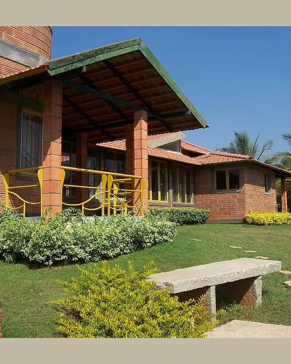 This farmhouse design uses hollow clay blocks and a sloping Mangalore tile roof to create a modern home with a strong vernacular feel. The open verandah and stone bench invite outdoor living, blurring the lines between the house and the lawn.