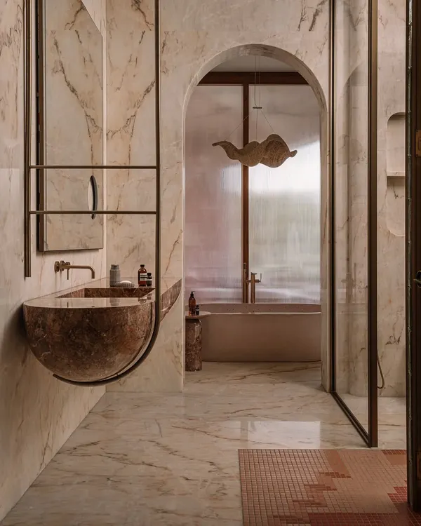 This junior master ensuite at Rehethaan is a moody, atmospheric space. A sculptural red marble sink appears to float, framed by an arched niche that leads to a private bathtub area.