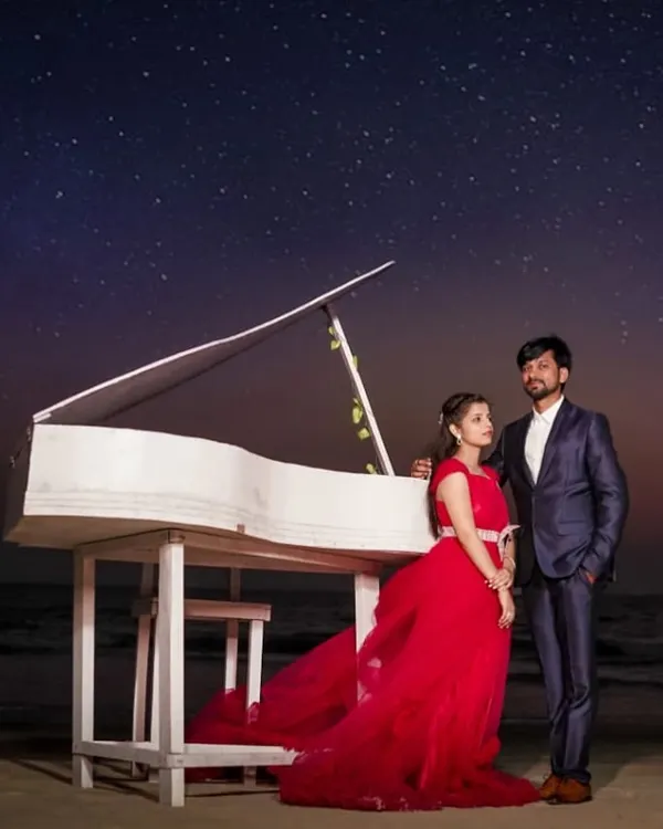 A magical pre-wedding night shoot on the beach. This couple used a piano prop under a starry sky, with the red trail gown adding a touch of vibrant, romantic color.