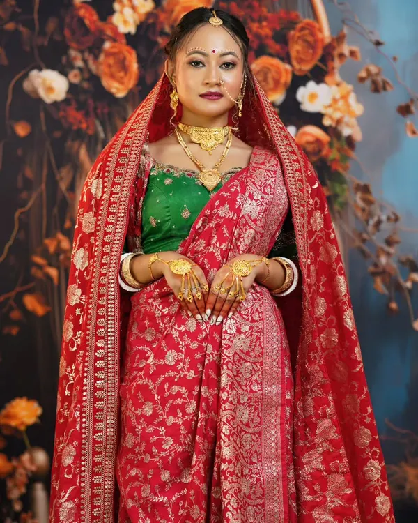 A full-length view of a traditional Bengali bride, showcasing the rich red Banarasi saree and the unique way of draping the veil.
