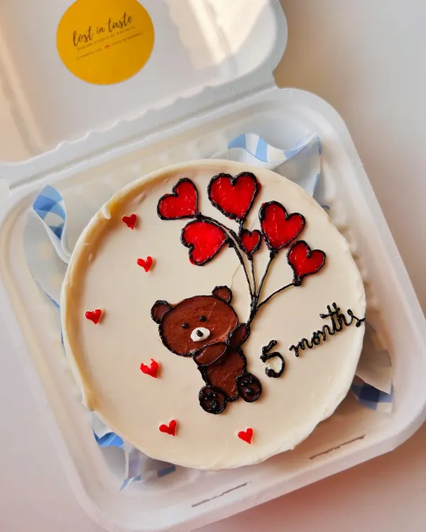 A sweet bento cake for a 5-month celebration, featuring a hand-piped teddy bear holding a bouquet of heart-shaped balloons.