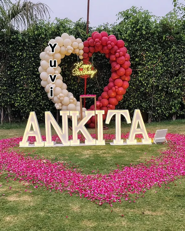 Make a statement with a grand outdoor decoration. This setup in a garden features large, light-up marquee letters spelling a name, a heart-shaped balloon arch, and a huge heart made of rose petals on the grass.