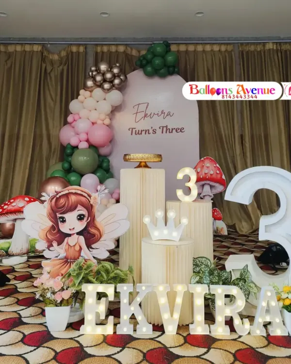 We create magical birthday experiences with fully themed decorations. This enchanting fairy setup includes a custom backdrop, a multi-colored balloon arch, marquee letters spelling the name 'Ekvira', themed cutouts like a fairy and mushrooms, and illuminated props to bring the scene to life.