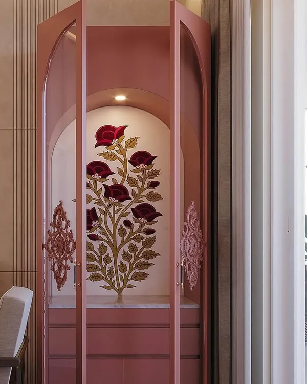 This custom pooja unit in a soft pink finish features arched glass shutters and intricate floral artwork, creating a beautiful and modern sacred space.