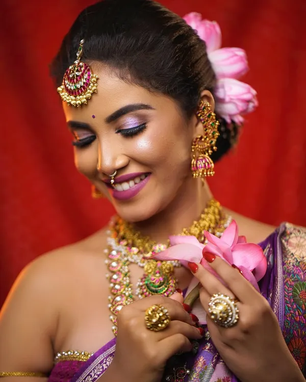 A beautiful bridal portrait where the hair is styled in a neat updo adorned with fresh lotus petals. This hairstyle allows the focus to be on the bride's expression and her intricate jewelry.